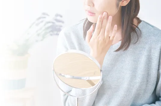 鏡を見ながら頬のふくらみを気にする女性